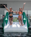 Two children sliding down a green and white inflatable water slide into a pool.
